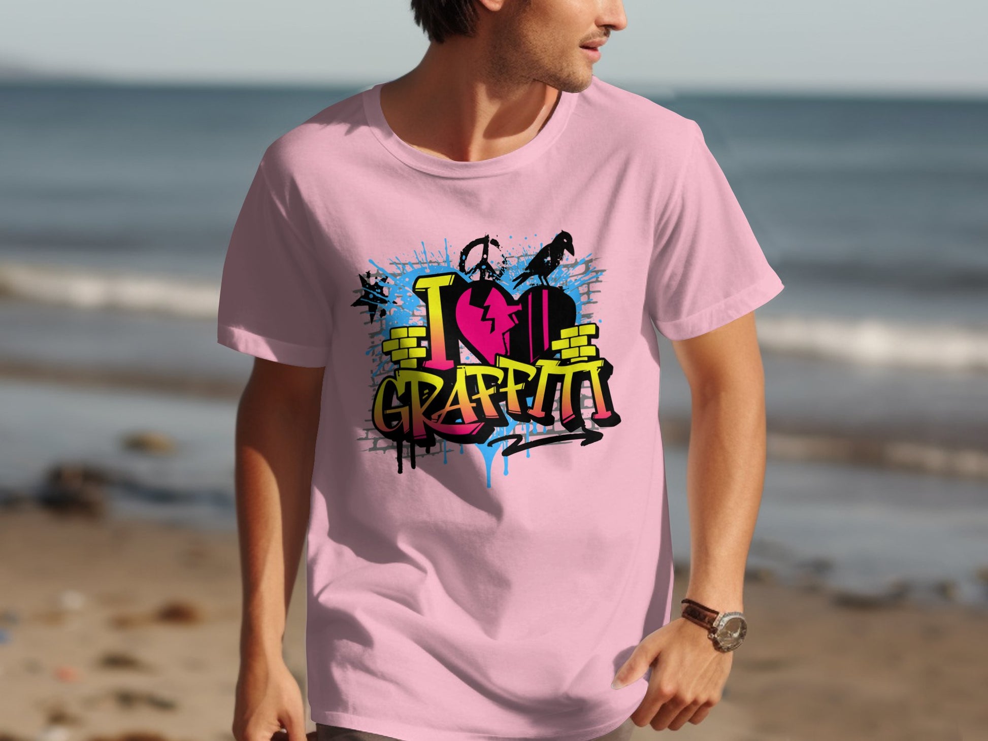 On the beach, someone wears a light pink T-shirt by Garment Graphics, featuring a vibrant I ♥️ Graffiti graffiti design. This street art-inspired piece embodies the spirit of Graffiti Love T-Shirts, with waves visible in the background.