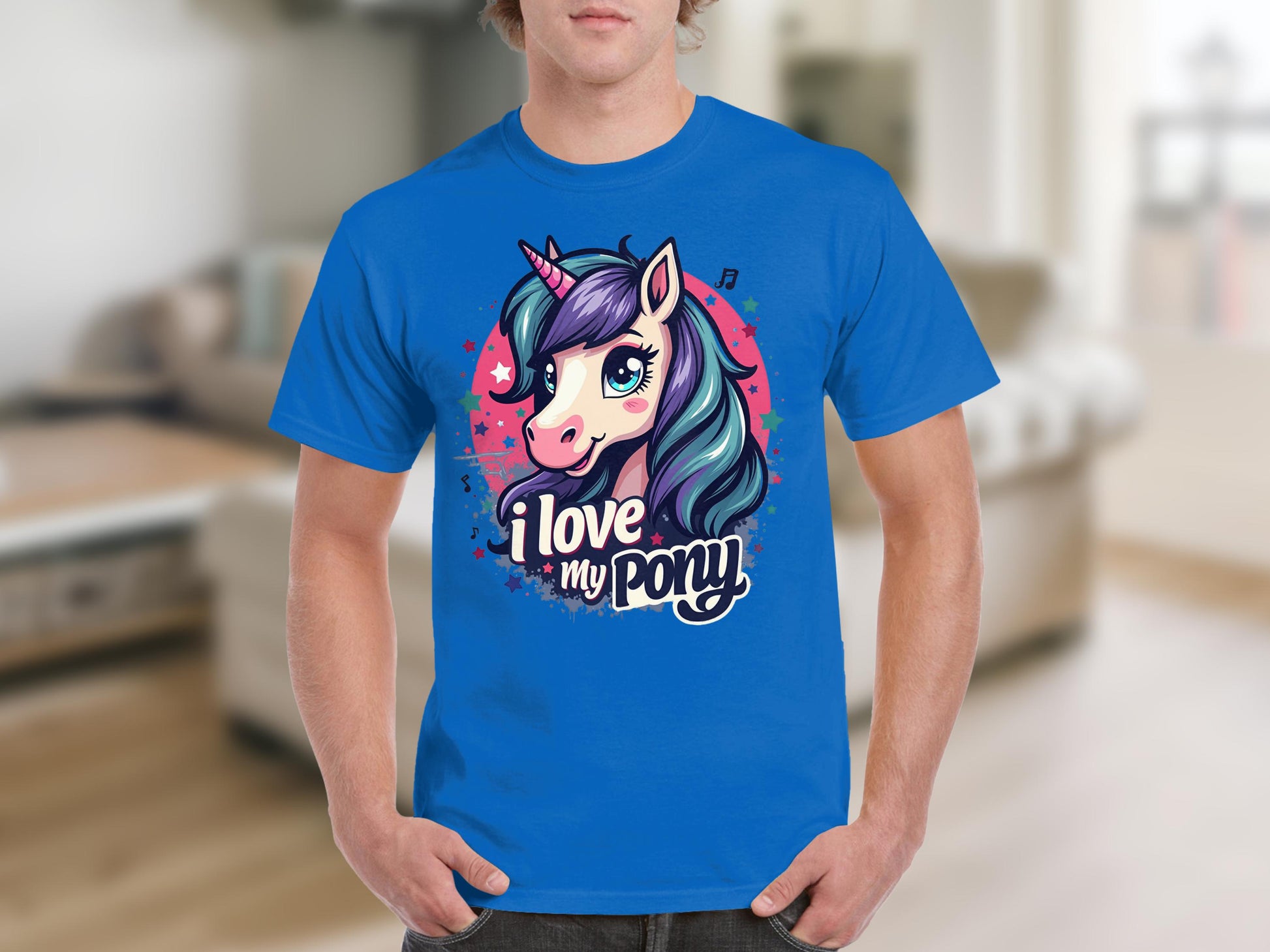 A unicorn fan wears a bright blue Garment Graphics T-shirt showcasing a big-eyed cartoon unicorn with a vibrant mane, alongside the text I love my pony, set against a blurred indoor background.