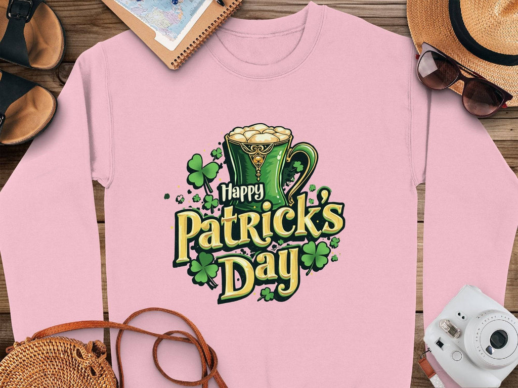 This pink long-sleeve shirt from Garment Graphics features a festive design with a green beer mug and shamrocks. It reads Happy Patricks Day and is displayed on a wooden surface alongside a hat, sunglasses, camera, sandals, and notebook.