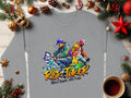 Urban-style gray sweatshirt by Garment Graphics with street dance graphics of two dancers in colorful clothing, spray paint effects, and the text Risk Taker, Street Dance 10th Final. Unisex sizing. Displayed on a wooden surface with festive decor and a coffee cup.