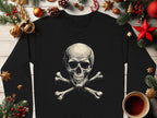 A Garment Graphics black long-sleeve shirt with a skull and crossbones design is styled on a wooden surface with festive decorations, including pine branches, pinecones, orange slices, a candy cane, ornaments, and a cup of black coffee.