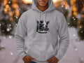 A person wears a light gray Garment Graphics Freebird Graphic Pullover Hoodie, adorned with an eagle with spread wings. This distinct style contrasts with a snowy backdrop and blurred lights, capturing the spirit of freedom and adventure.