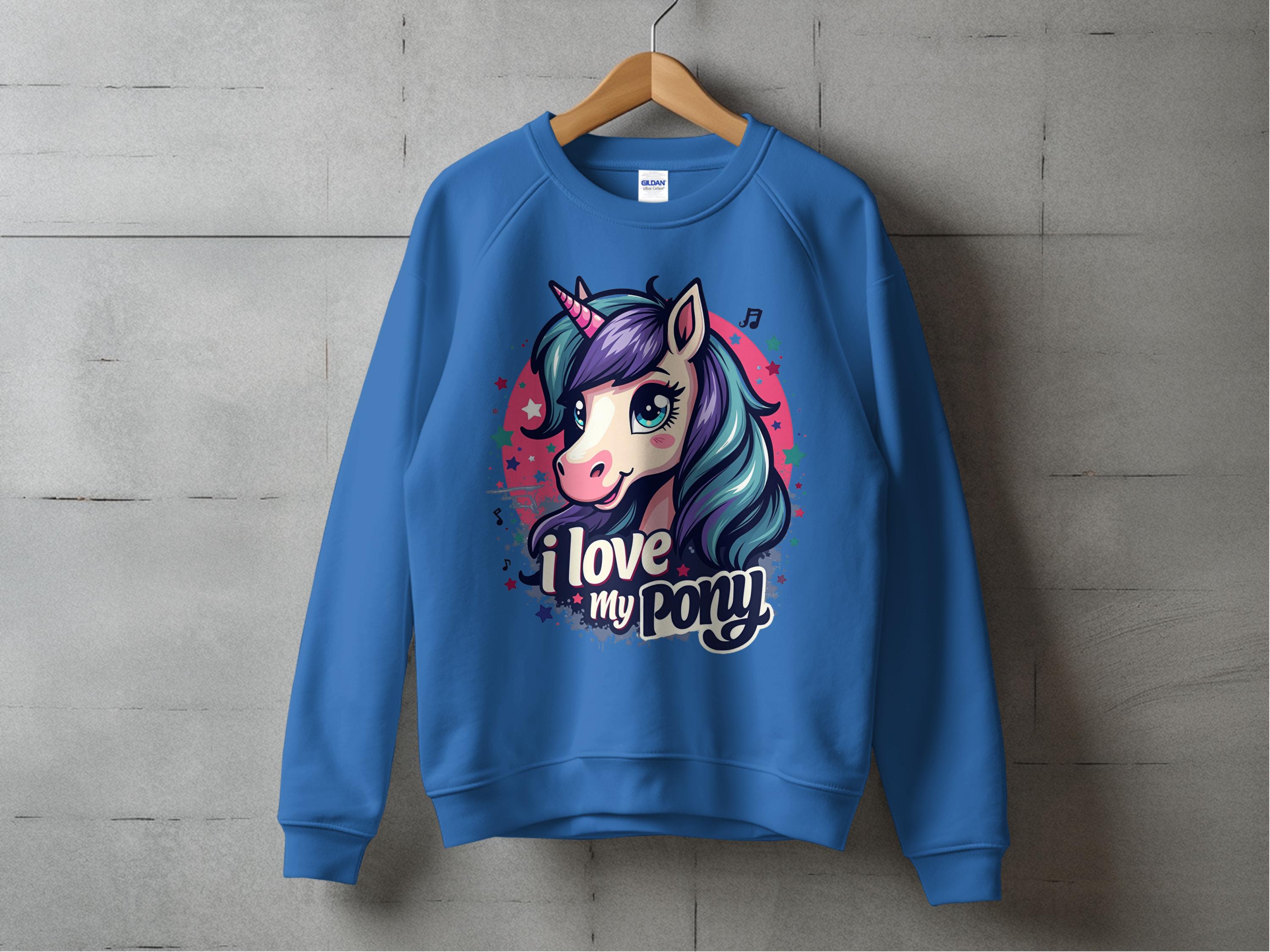A blue Garment Graphics sweatshirt features a vibrant pony-unicorn design with large eyes and a flowing mane, accompanied by the text I love my pony, hanging against a concrete wall.