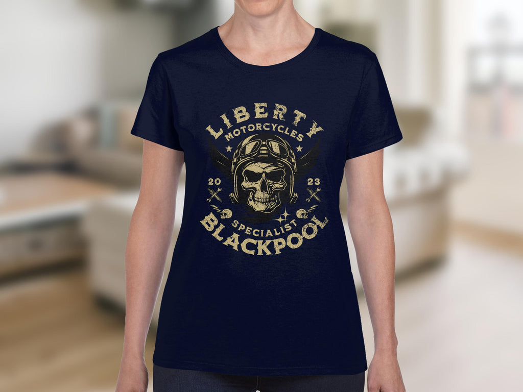 Someone is wearing a Garment Graphics navy t-shirt featuring a skull and wings design with Liberty Motorcycles Specialist Blackpool 2023 encircling it, standing out in the softly focused indoor setting.