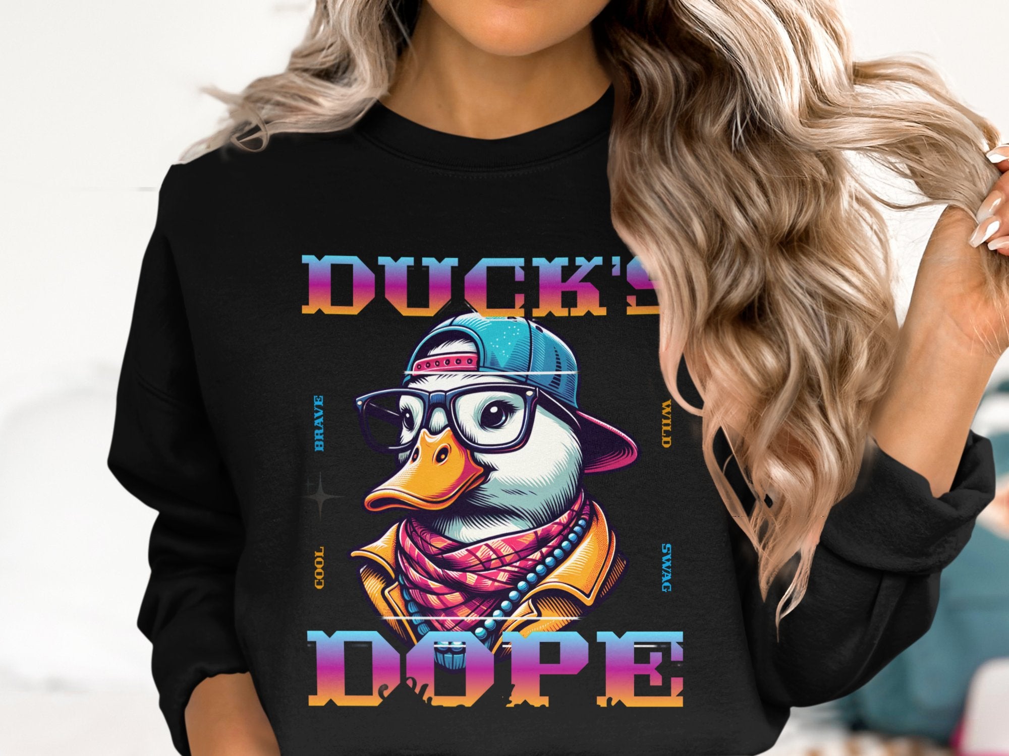 A person with long, wavy hair confidently wears a bold black sweatshirt by Garment Graphics. It showcases a cool cartoon duck in a cap, glasses, and patterned scarf, while vibrant gradient letters spell Ducks Dope, making this piece a standout fashion statement.