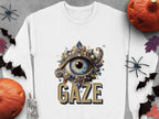 Garment Graphics presents a white sweatshirt with a jewel-encrusted eye above GAZE, surrounded by bats, spiders, black leaves, a skeleton, and jack-o-lanterns on a gray background. Available in unisex sizes, its a timeless style staple.