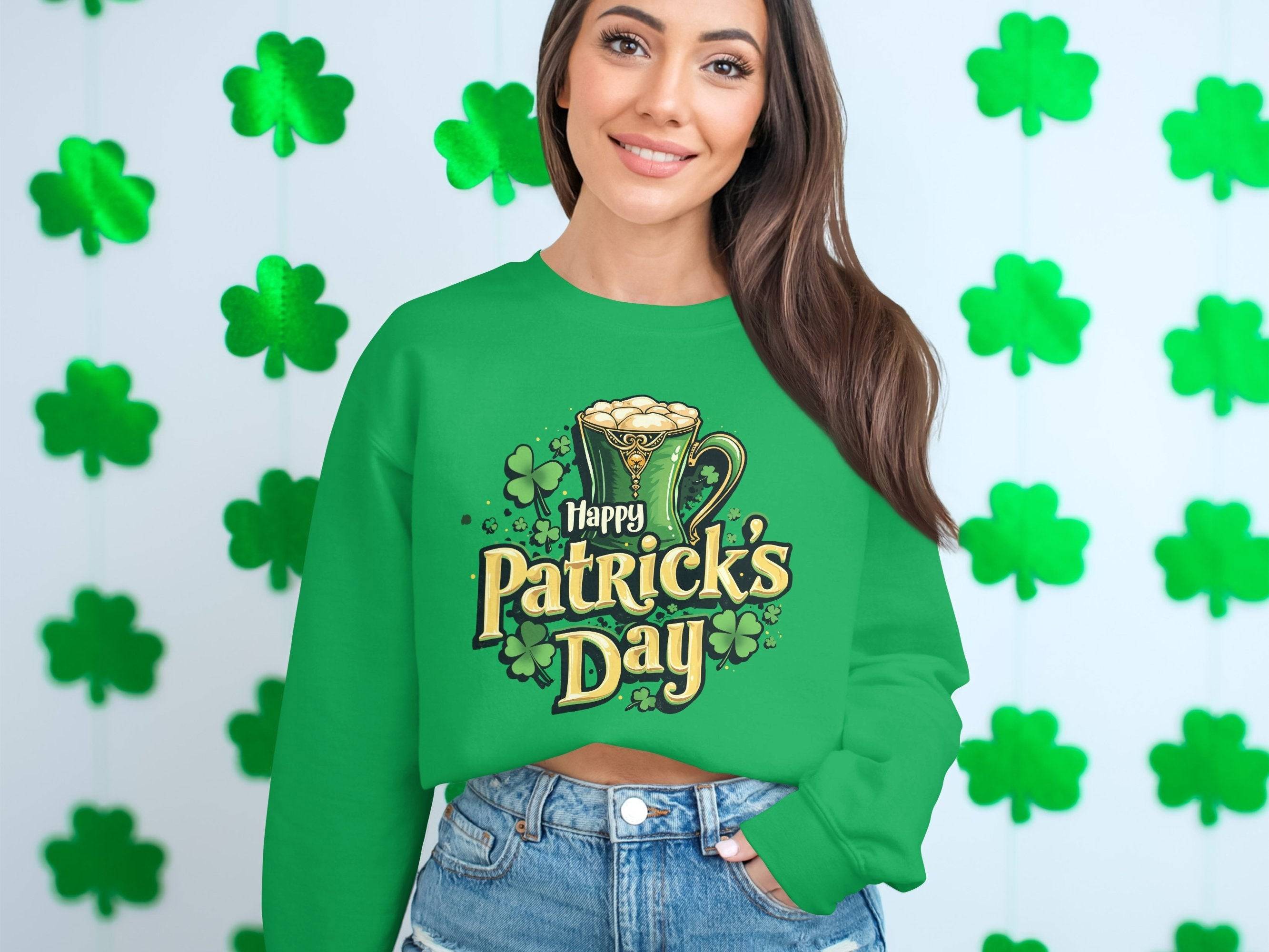 A person wearing a vibrant St. Patricks Day sweater by Garment Graphics, featuring a festive beer mug and shamrocks, stands before a wall adorned with green shamrocks. With long hair flowing and denim shorts completing the look, they effortlessly embody the holiday spirit.
