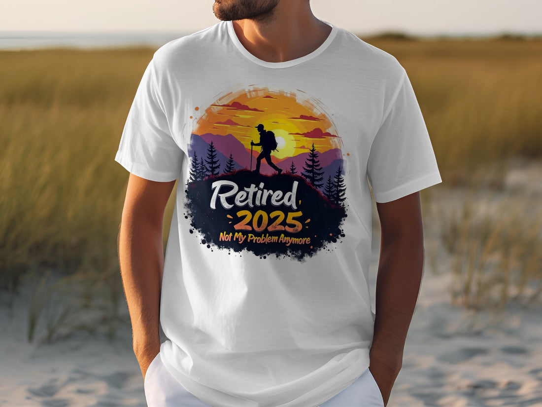A person is wearing a Garment Graphics white T-shirt featuring a colorful design of a hiker silhouette with mountains and trees, alongside the text Retired 2025 Not My Problem Anymore, embodying retirement vibes. A grassy area sets the backdrop for this lively scene.