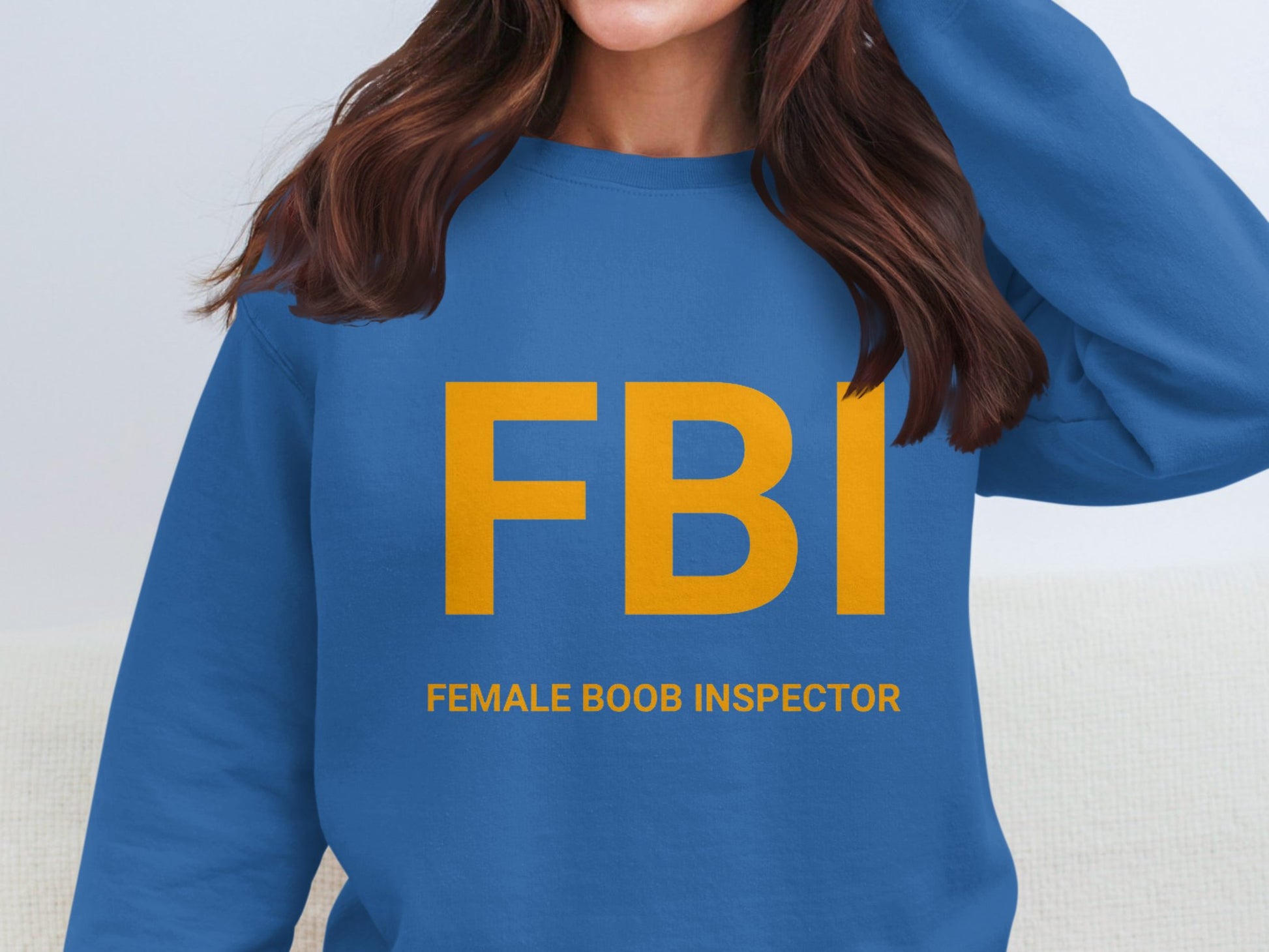 Someone is wearing a Garment Graphics blue sweatshirt with large yellow FBI letters and smaller text Female Boob Inspector. Only the lower face and torso are shown, indicating a unisex fit for this playful apparel.