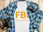A flat lay image from Garment Graphics displays a white sweatshirt with FBI Female Boob Inspector in bold orange letters, accompanied by a blue plaid shirt, headphones, camera, and to-go coffee cup on wood. This playful piece offers unisex sizing for versatile style options.