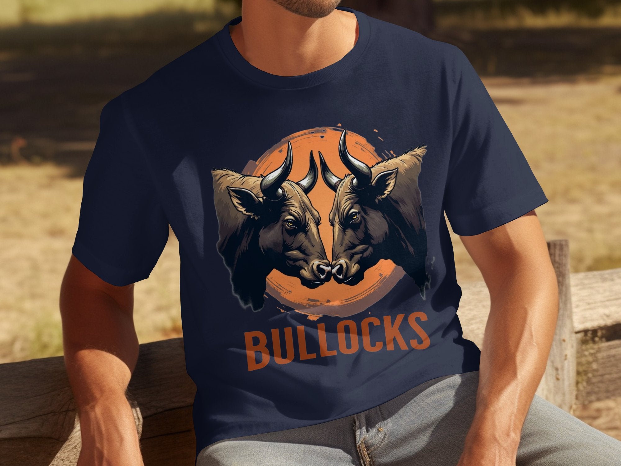 On a wooden bench outdoors, someone wears a dark blue, classic fit t-shirt from Garment Graphics featuring two bull heads facing each other with BULLOCKS below, blending comfort and style amid grass and trees.