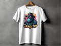 A white Garment Graphics t-shirt hangs on a wooden hanger against a gray backdrop, featuring a vibrant graphic of a gorilla in sunglasses, hat, and jacket with Gangster below. This classic fit Gangster Gorilla T-Shirt effortlessly embodies urban style.