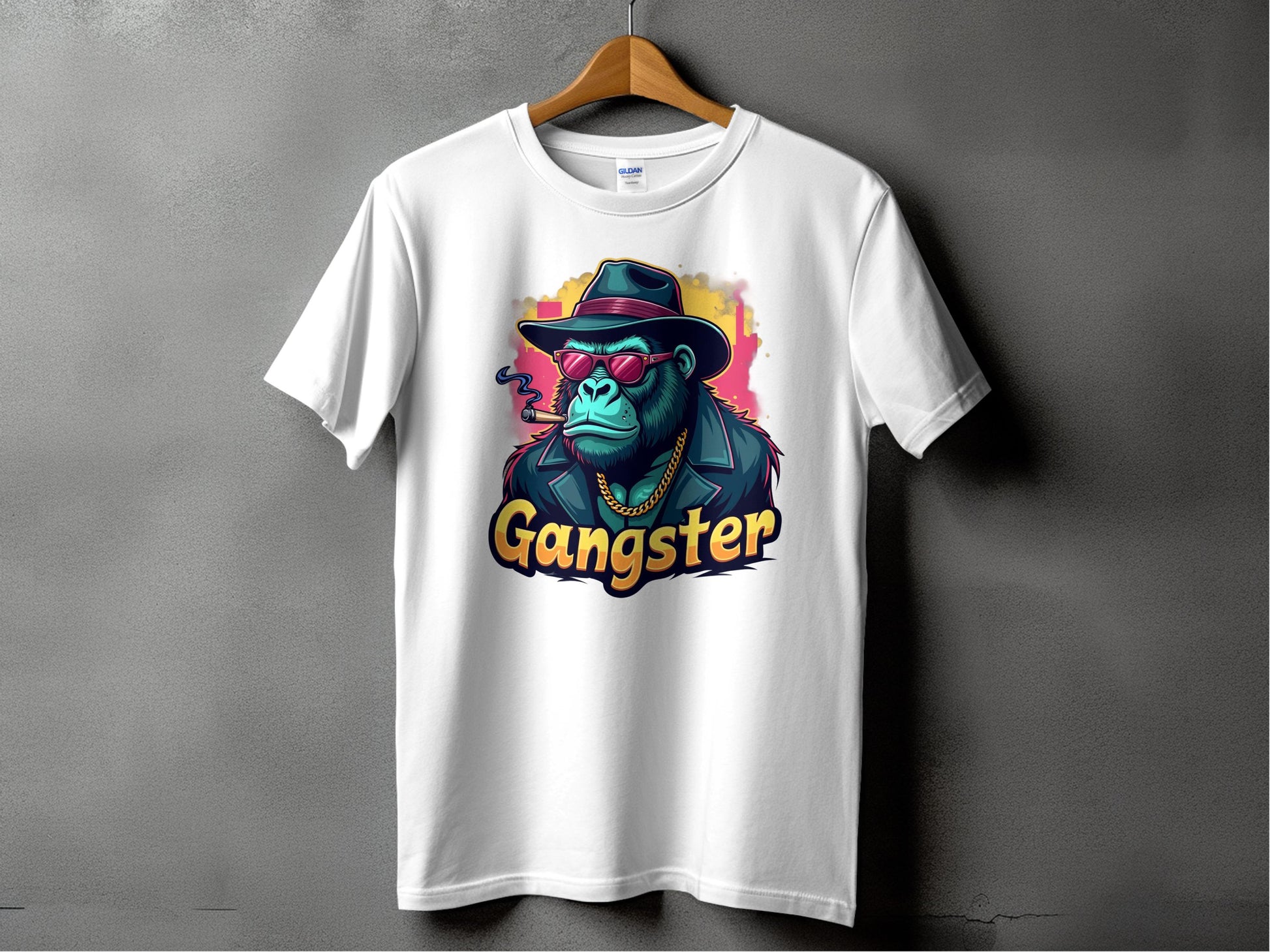 A white Garment Graphics t-shirt hangs on a wooden hanger against a gray backdrop, featuring a vibrant graphic of a gorilla in sunglasses, hat, and jacket with Gangster below. This classic fit Gangster Gorilla T-Shirt effortlessly embodies urban style.