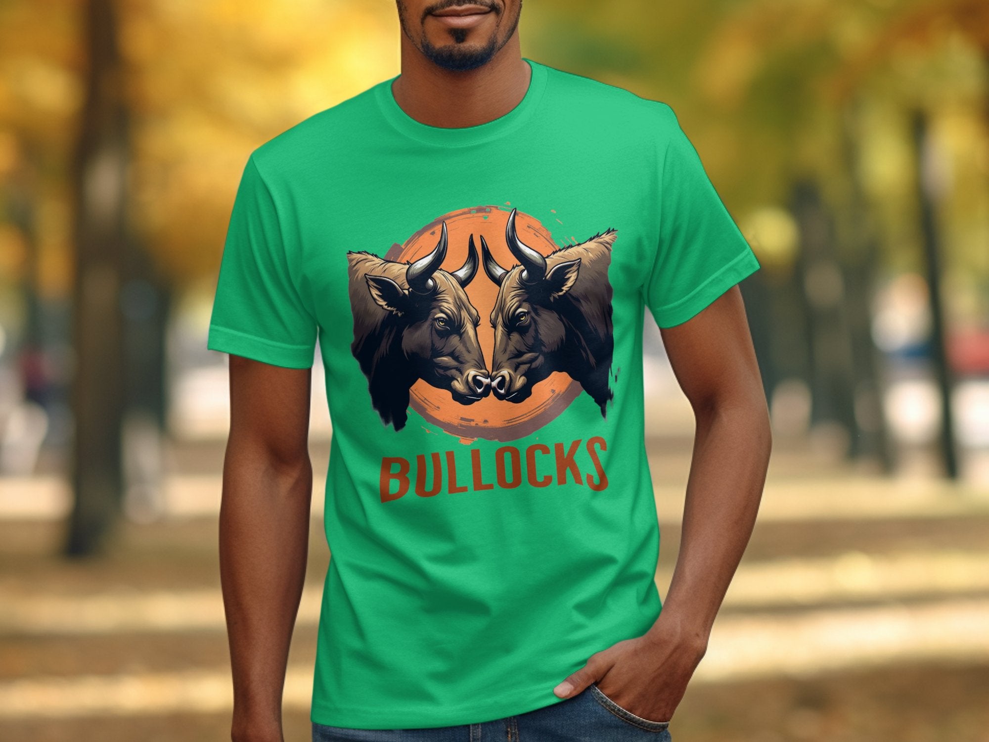 A person wears a Garment Graphics classic fit green T-shirt with two angry bulls facing each other above BULLOCKS. Theyre in a park with vibrant autumn trees, ideal for family outings and flaunting your Bullocks Pintable T-Shirts style.