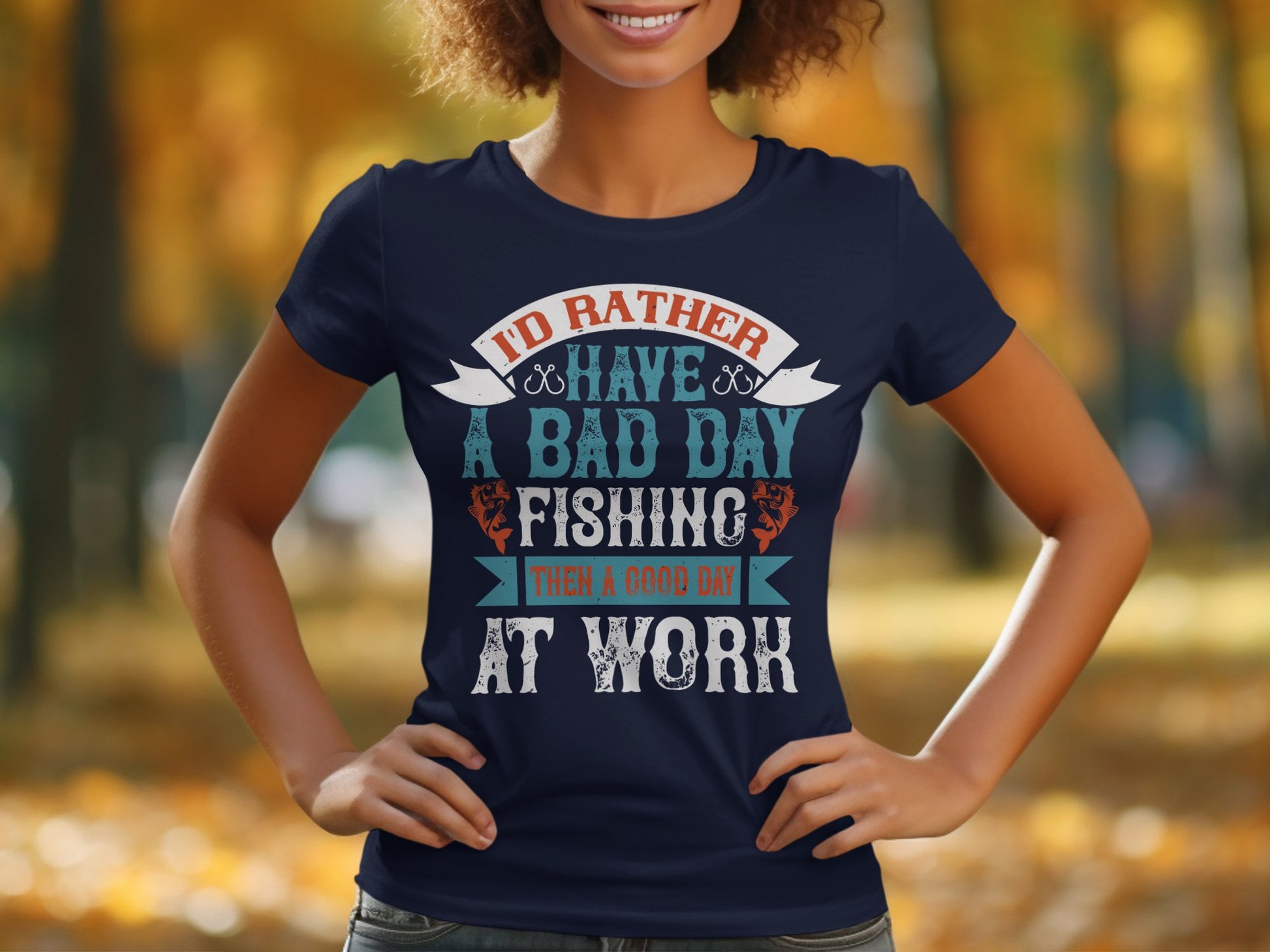 A person is outdoors in a Garment Graphics womens navy blue fishing T-shirt that reads: ID RATHER HAVE A BAD DAY FISHING THAN A GOOD DAY AT WORK. The background features blurred autumn trees, perfect for fishing enthusiasts.