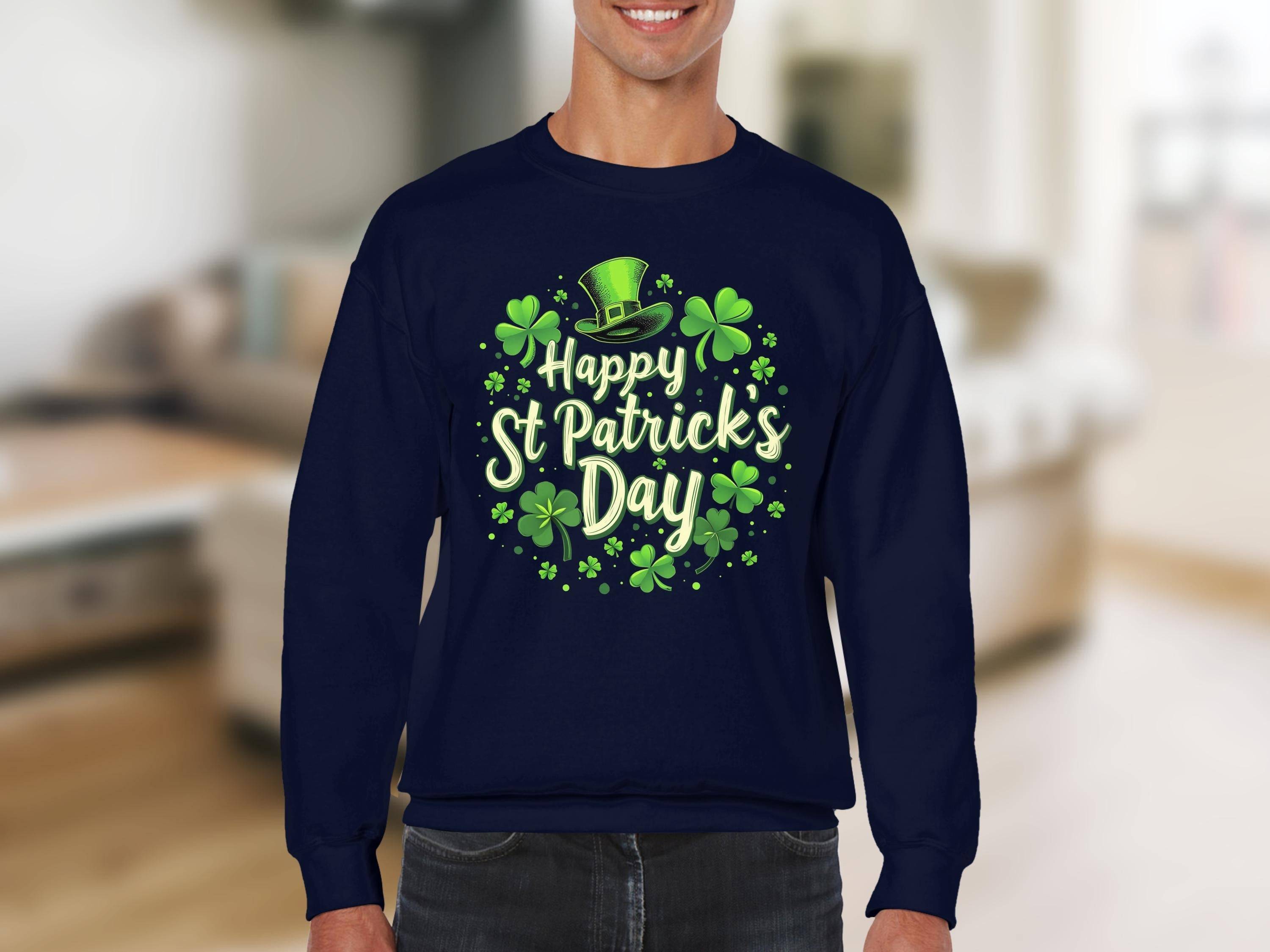 A person celebrates festive cheer in a navy blue Garment Graphics sweatshirt featuring a vibrant St. Patricks Day shamrock graphic with a green top hat and Happy St. Patricks Day text in green and white, set against a blurred interior background.