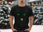 Wearing a Garment Graphics Happy St. Patricks Day black graphic T-shirt with green clovers, a person brings festive flair to snow-covered trees, hands in their jeans, blending holiday cheer with winters beauty.