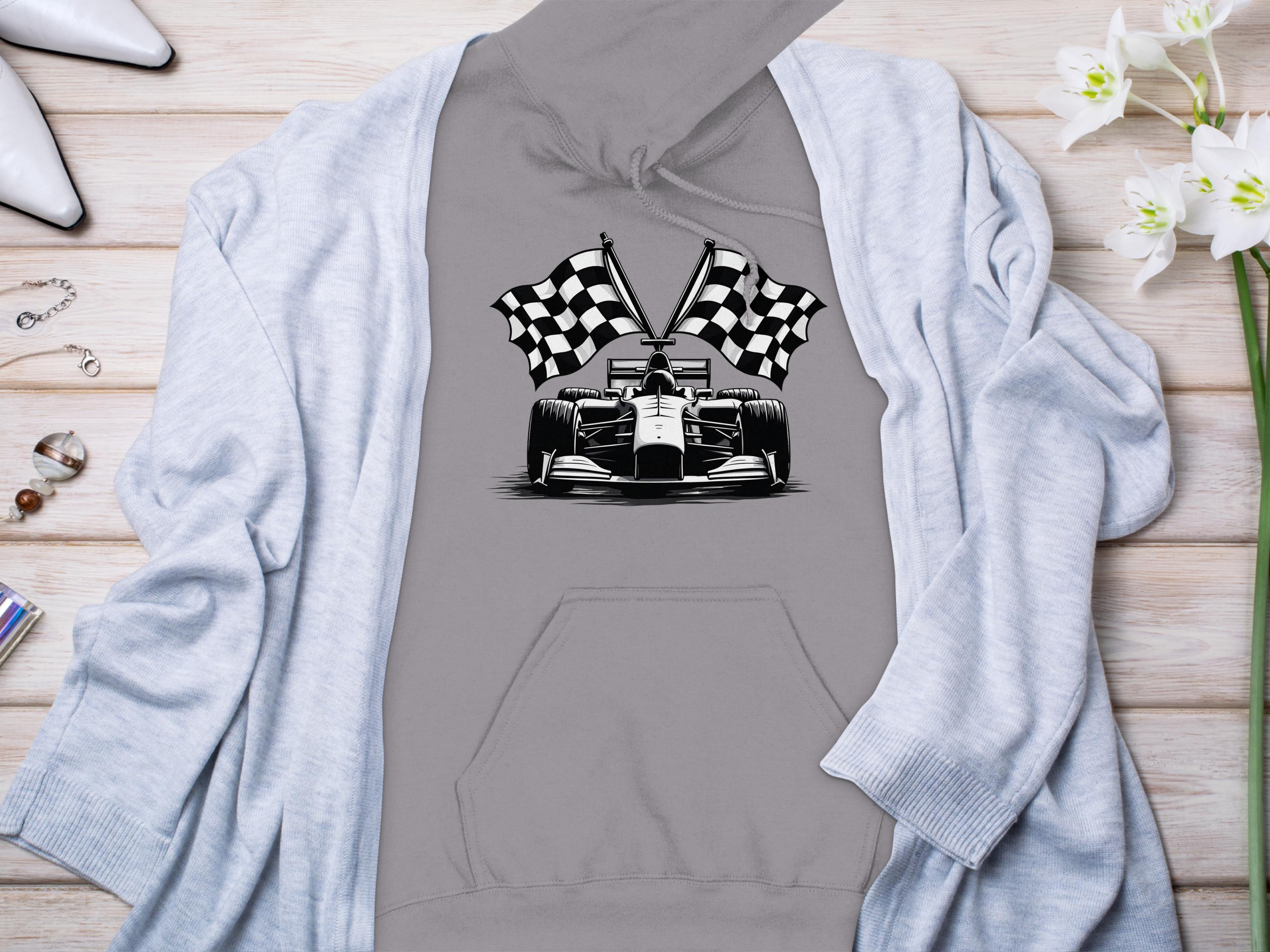 A grey Garment Graphics racing-themed hoodie features a race car graphic with checkered flags on a wooden surface, surrounded by a light blue cardigan, white high-heeled shoes, white flowers, and small jewelry items.