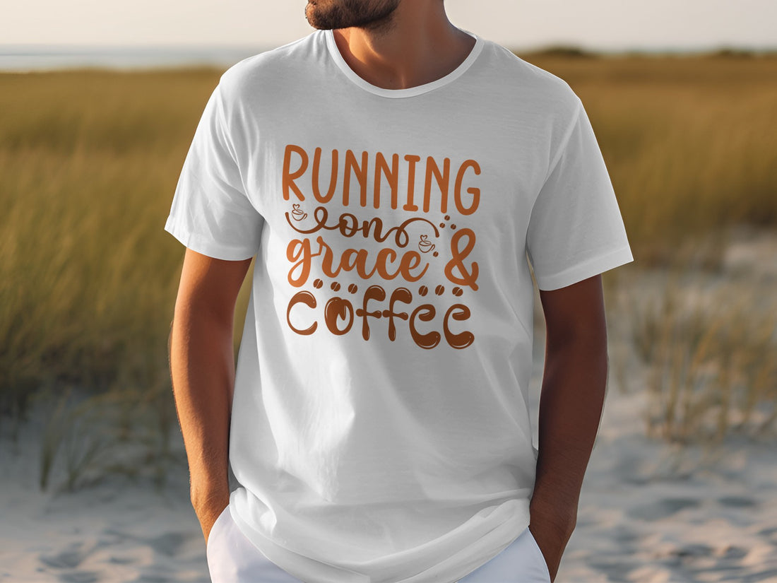 A person sits outdoors in a Garment Graphics T-Shirt with Running on grace & coffee in orange, set against a sandy terrain and tall grass.