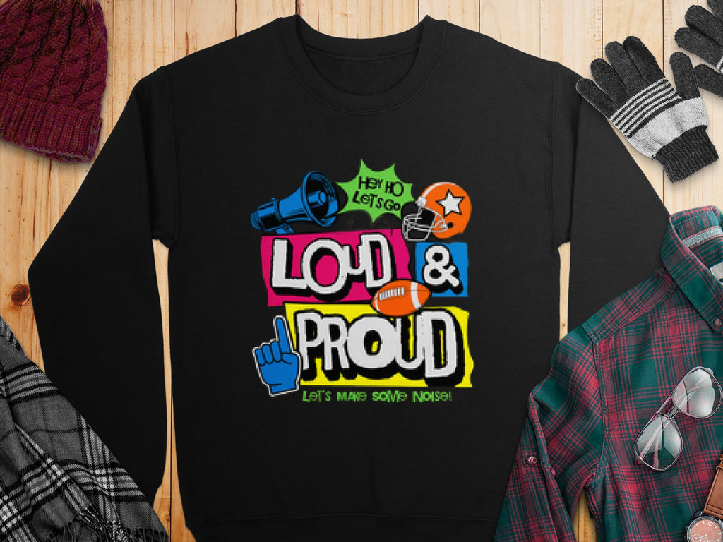 A unisex black sweatshirt from Garment Graphics features the vibrant Hey Ho Lets Go Loud & Proud design, showcasing megaphone, foam finger, football, and helmet graphics. Its part of the unique style of Loud and Proud Sweatshirts, set against a wooden backdrop with a hat and gloves.