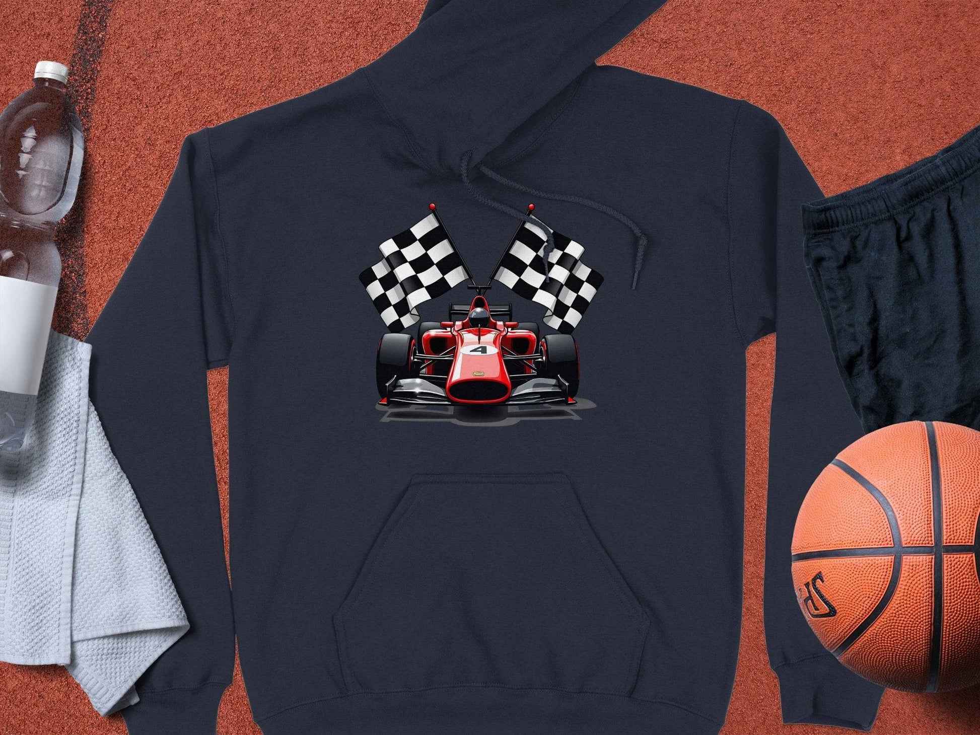 Garment Graphics dark hoodie showcases a red racing car with checkered flags, surrounded by essentials like a water bottle, white towel, black shorts, and an orange basketball on a rust-colored surface.