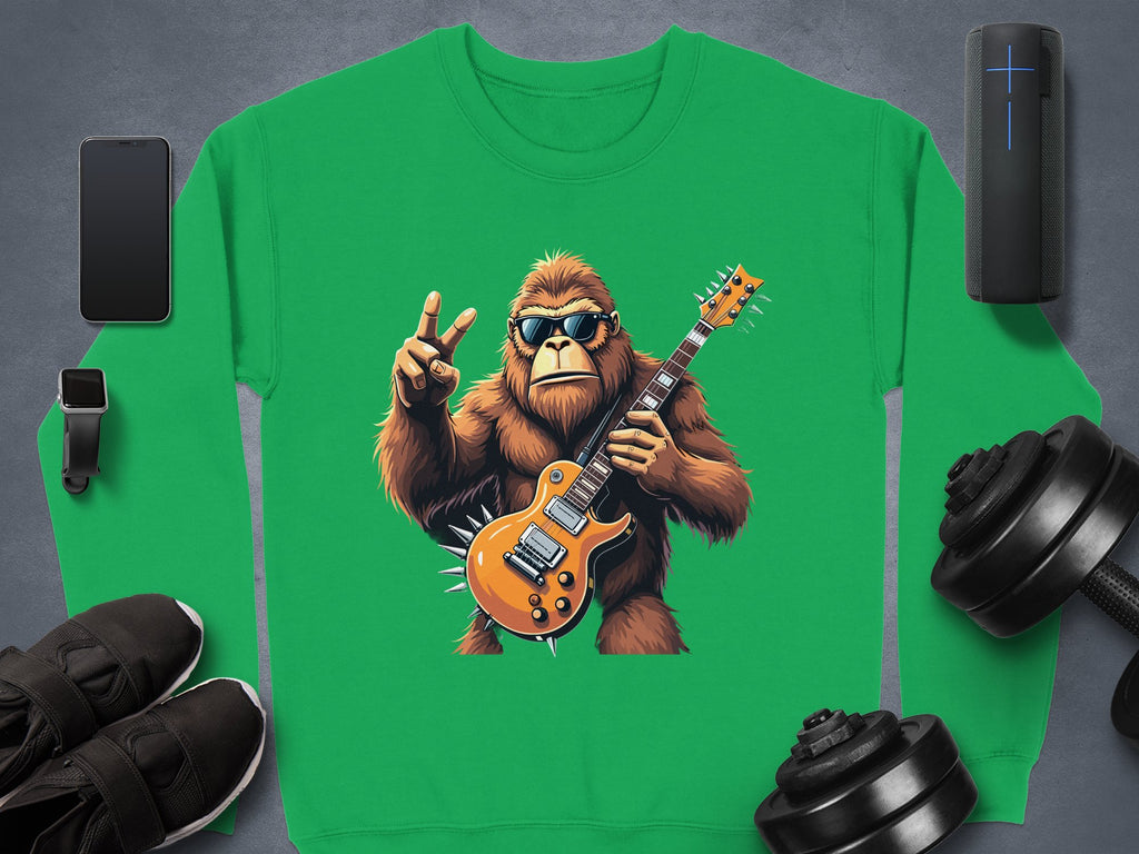 Garment Graphics offers a green rocking gorilla sweatshirt with a gorilla in sunglasses, holding an electric guitar and flashing a peace sign. Ideal for stylish music lovers; nearby items include smartphone, wireless speaker, smartwatch, black shoes, and dumbbells.