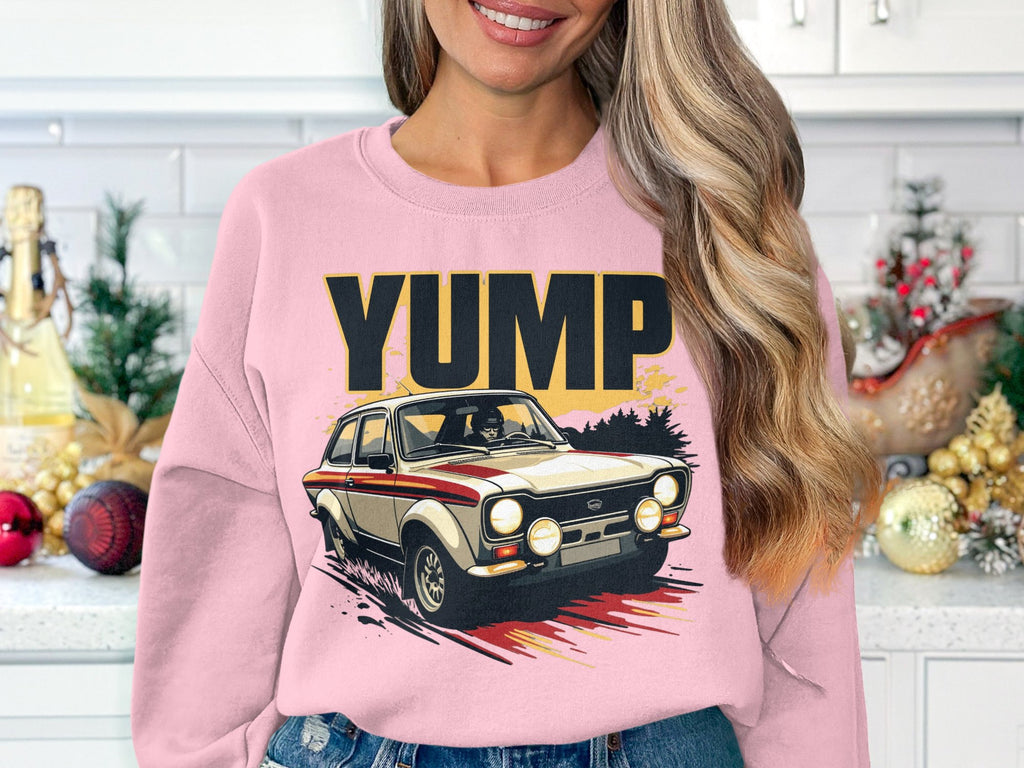 A woman with long hair dons a pink Garment Graphics sweatshirt featuring a YUMP rally car design in her kitchen, where holiday decorations scattered on the counter encapsulate the festive spirit.