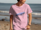 A man in a pink Garment Graphics shirt with a vibrant retro design walks along the beach. The classic fit tee, featuring RETRO in colorful letters, adds vintage charm as he strolls by the ocean and sand.