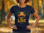 In a park-like setting, someone wears a Garment Graphics navy T-shirt featuring two palm trees, an airplane, and a tropical sunset. The words One Love evoke a carefree beach outing vibe amidst the backdrop of blurred autumnal trees glowing with warm yellow and orange leaves.