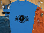 A Garment Graphics blue t-shirt with Scania 8 Power text and graphic design on a wooden surface, surrounded by wireless headphones, denim hat, sunglasses, blue jeans, orange shirt, wristwatch, and keys.