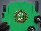 A Garment Graphics green sweatshirt with an Irish spirit boasts a shamrock design encircled by smaller ones. It is displayed on a gray surface alongside a smartphone, smartwatch, speakers, black sneakers, and weights.