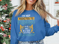 A person wearing a Garment Graphics blue unisex sweatshirt with Im not addicted to fishing, we are just in a very committed relationship printed on it stands before a decorated Christmas tree.