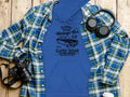 A blue Garment Graphics hoodie with a London vintage car design and classic car club text rests on a wooden surface, paired with a plaid shirt, headphones, and a camera—ideal for automobile enthusiasts with a classic fit style.