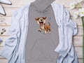 This playful Garment Graphics gray hoodie, perfect for dog lovers with its cartoon dog design, is displayed on a wooden surface. Its attractively complemented by a light gray cardigan, white pointed shoes, jewelry, and a bouquet of white flowers.