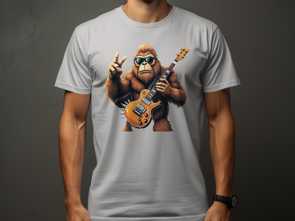 A person wears a Garment Graphics white T-shirt with Bigfoot, looking like a chill gorilla in sunglasses, holding an electric guitar and making a peace sign. Perfect for music lovers, the design rests on a plain dark gray background.