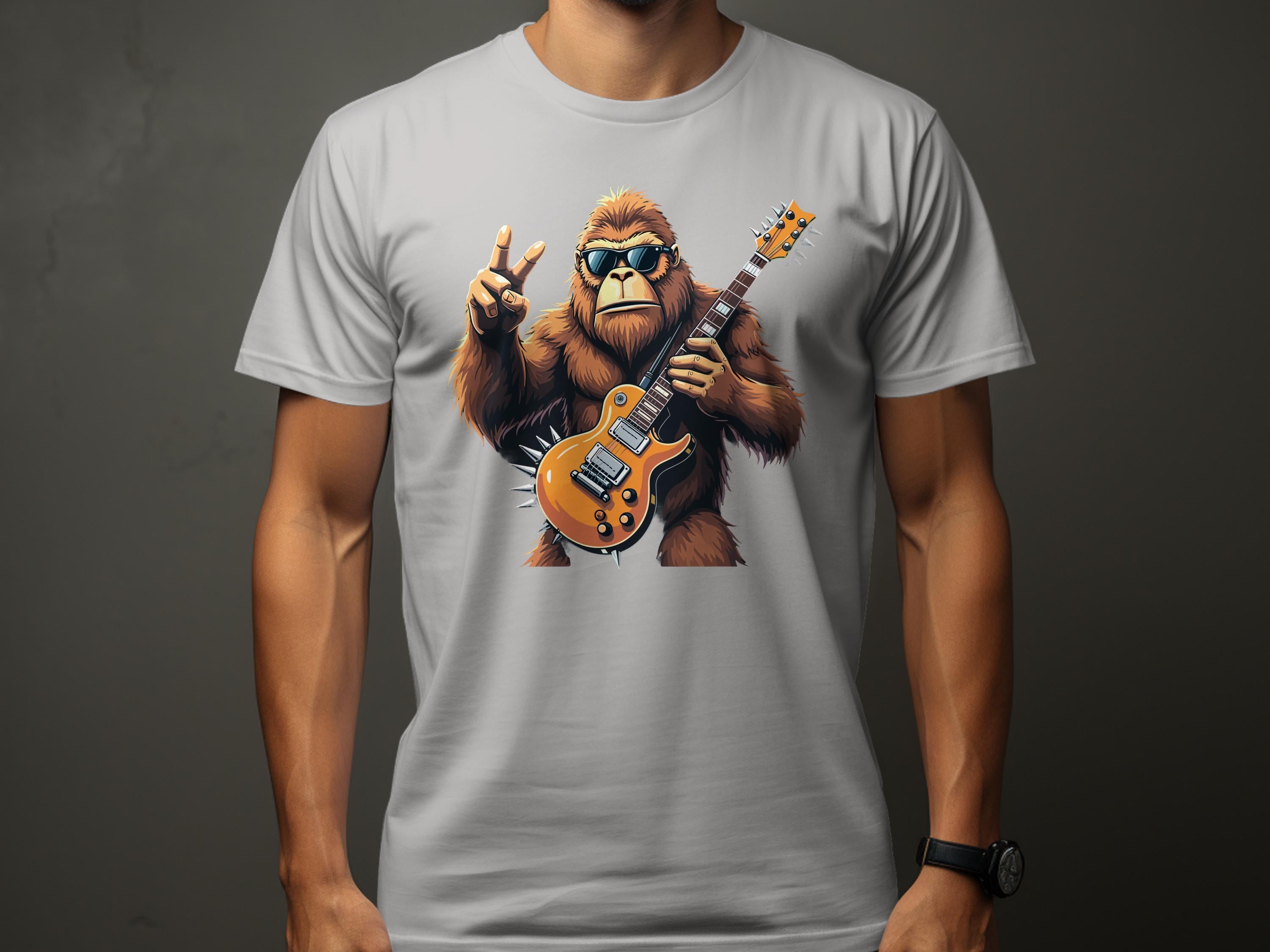 A person wears a Garment Graphics white T-shirt with Bigfoot, looking like a chill gorilla in sunglasses, holding an electric guitar and making a peace sign. Perfect for music lovers, the design rests on a plain dark gray background.
