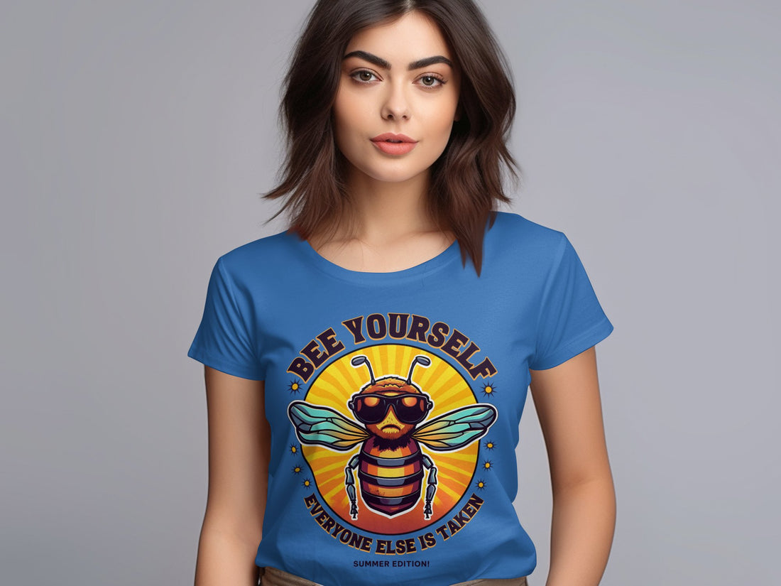 A woman with brown hair wears a blue Garment Graphics Bee Yourself T-Shirt featuring a cartoon bee in sunglasses. The text reads, Bee Yourself, Everyone Else is Taken, Summer Edition, designed for womens sizing against a plain gray backdrop.