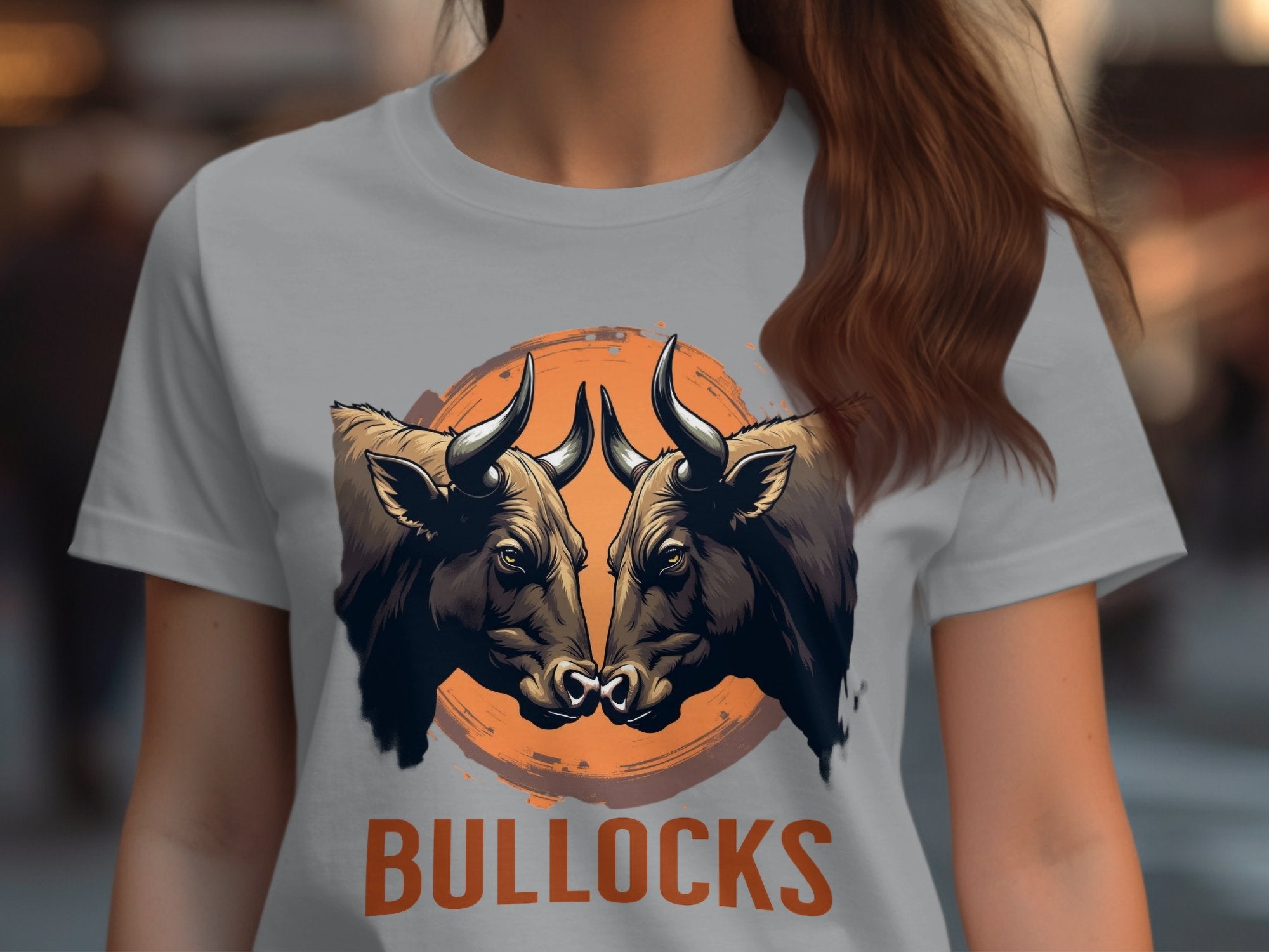 A person is wearing a Garment Graphics t-shirt with two bulls facing each other in an orange circle, BULLOCKS printed boldly below. The background is blurred, enhancing this striking casual wear.