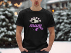 In a snowy outdoor scene, someone wears a Garment Graphics classic-fit black T-shirt with Soccer mum and a soccer ball graphic. Trees and snow create a scenic background.