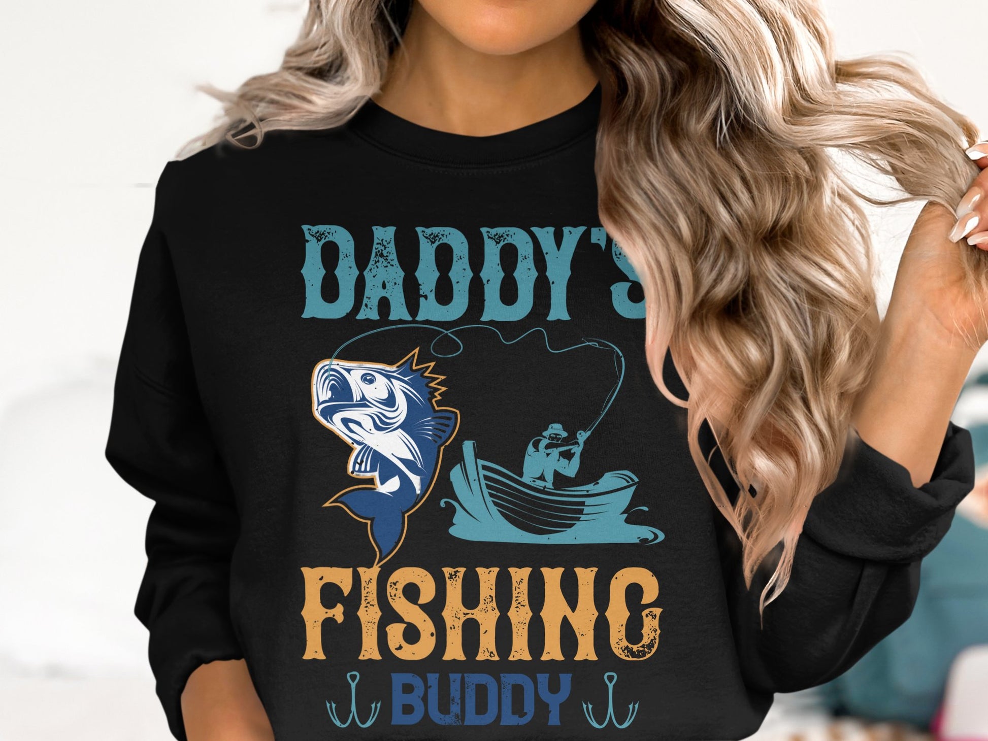 A person with long hair models a black fishing sweatshirt by Garment Graphics, featuring vibrant artwork of a fish and a boat with the text Daddys Fishing Buddy in various colors—a perfect nod for fishing enthusiasts.