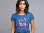 A woman with shoulder-length brown hair stands against gray, wearing a blue t-shirt from Garment Graphics stating Just be COOL Rock and Roll. Featuring white and pink headphones, its perfect for music lovers who appreciate headphone-themed tees.