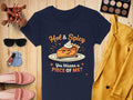 A Garment Graphics navy T-shirt showcases a pie slice with Hot & Spicy above and You Wanna a Piece of Me? below. Ideal for casual wear, its displayed with makeup, a yellow jacket, pink shoes, nail polish, and brushes on wood. Available in womens sizes.
