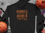 The Garment Graphics Running on Grace & Coffee black hoodie features bold orange text with playful pumpkins, bats, a skeleton, and a spider on a gray backdrop. This classic fit hoodie is crafted from medium-heavy fabric for comfort and style.