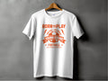 A white T-shirt from Garment Graphics hangs on a wooden hanger against a gray background, showcasing orange text and graphics. It features Born to Play above a football and the slogan One Goal - One Dream, ideal for passionate football fans.