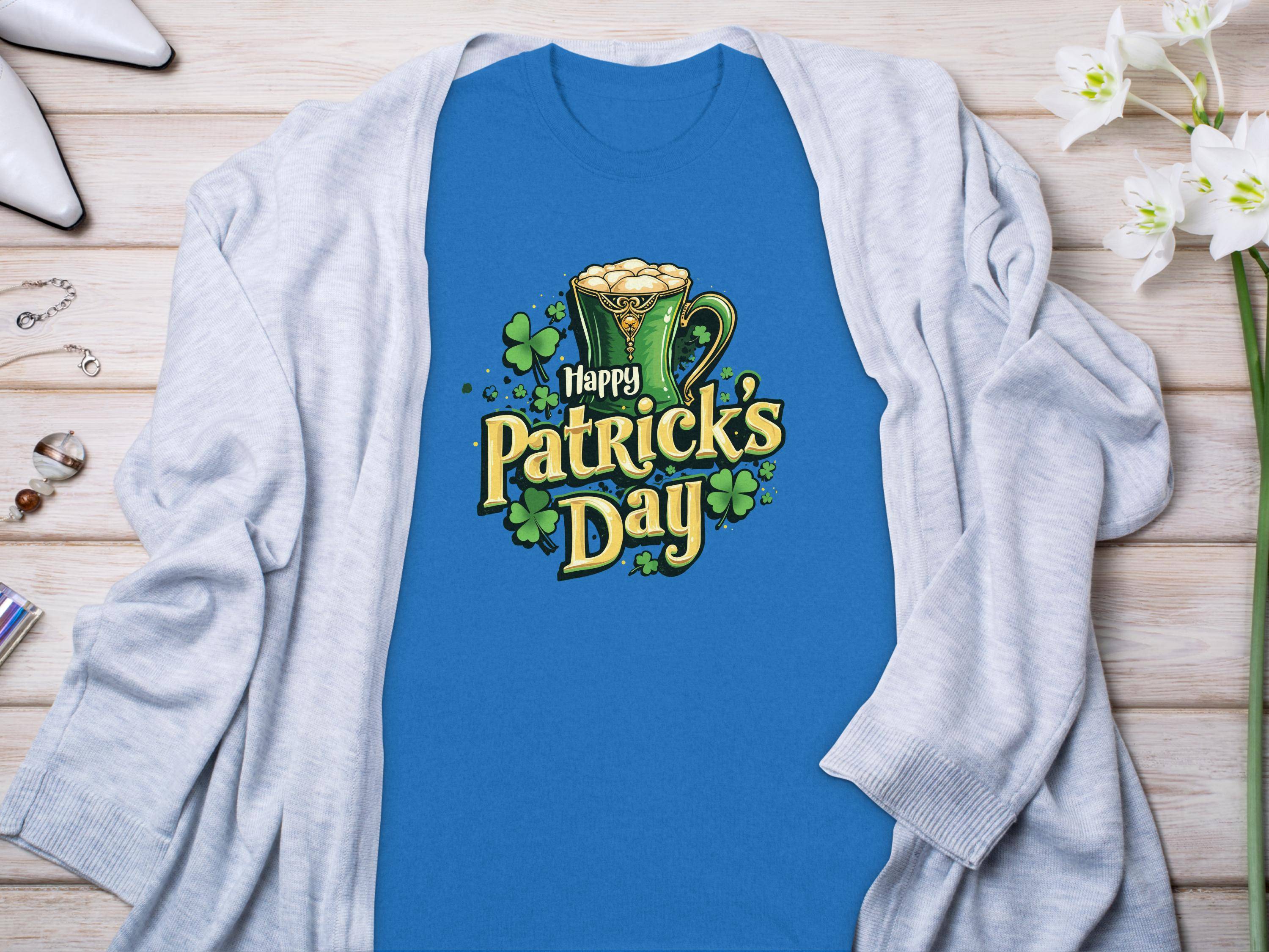 Celebrate Patricks Day with Garment Graphics T-shirt, showcasing decorative yellow text, green shamrocks, and a foamy beer mug illustration. Paired with a light gray cardigan on wood, its perfect for festivity accessorizing.