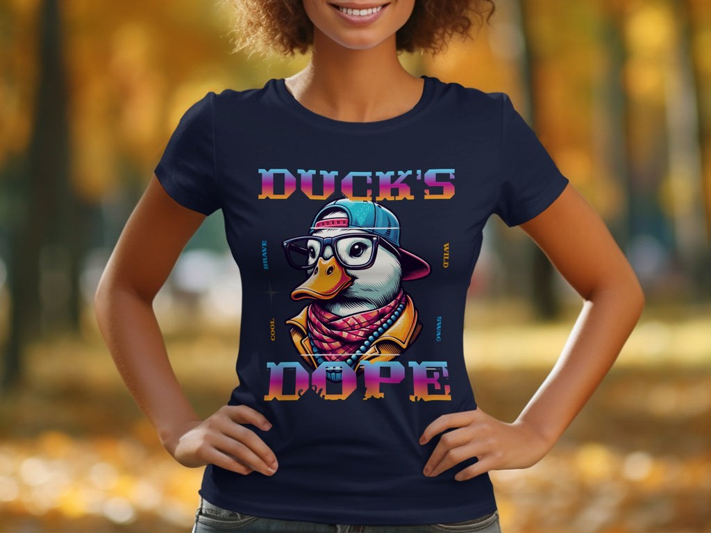 In a park with autumn foliage blurred in the background, someone wears a Garment Graphics T-shirt showcasing a cartoon duck with sunglasses and a cap. The design includes Ducks Dope text, creating a striking visual effect.