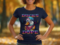 In a park with autumn foliage blurred in the background, someone wears a Garment Graphics T-shirt showcasing a cartoon duck with sunglasses and a cap. The design includes Ducks Dope text, creating a striking visual effect.