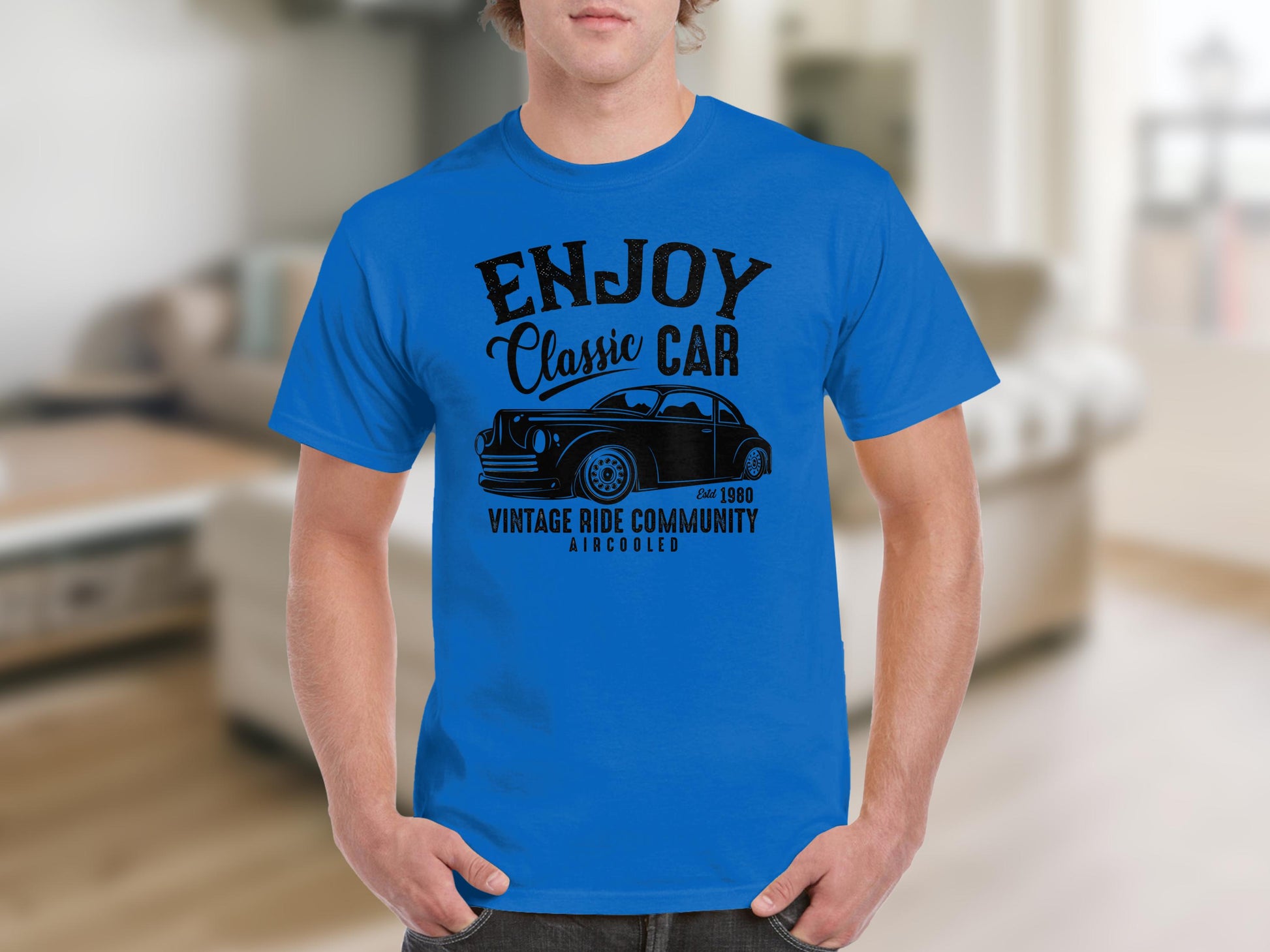 A man in a blue Garment Graphics T-shirt with a black classic car graphic and the text ENJOY Classic Car, Est. 1980, Vintage Ride Community, Aircooled stands against a blurred indoor backdrop. Ideal for vintage ride and classic car enthusiasts.