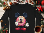 Garment Graphics presents a black long-sleeve shirt with a whimsical donut character sporting mouse ears and gloves on pink icing. Ideal for the holiday season, its surrounded by festive decor such as pine cones and cinnamon sticks, available in unisex sizing like cozy sweatshirts.