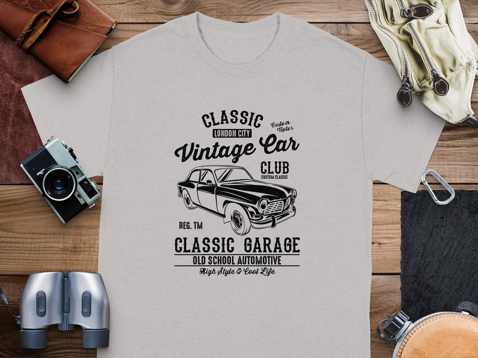 The Garment Graphics light gray t-shirt features a black vintage car graphic and text reading Classic Vintage Car Club, London City, Classic Garage, Old School Automotive. Its crafted in a classic fit style with details like a camera, compass, and leather item for a retro automotive vibe.